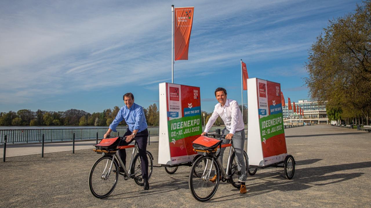 Herr Dr. Volker Schmidt und Herr Krach auf Fahrrädern mit Plakat-Anhänger